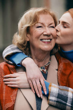 A happy grandmother and granddaughter hugging and kissing outside.