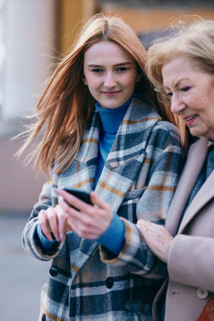 A grandmother and her grandchild standing on the street and reading messages on the phone.