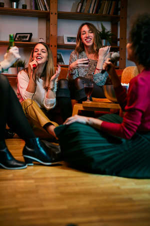 Happy multicultural friends sitting at home, laughing, singing, and having fun on karaoke night.の写真素材