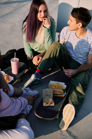 A small group of teenagers sitting outdoors and having fast food for a snack. Urban teenagers hanging out after school.の写真素材