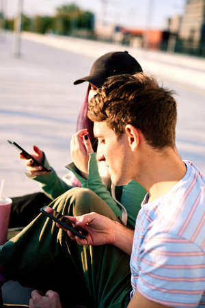 Two teenagers addicted on social media sitting in urban exterior and using phones.の写真素材