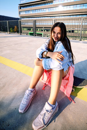 A teenage skater girl sits at the train station on the skateboard and smiles at the camera.の写真素材
