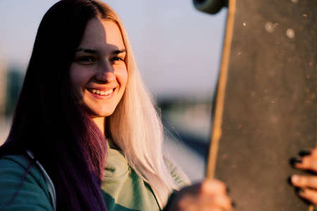 Portrait of a teenage skater girl holding skateboard towards sun and making shadow on her face.の写真素材