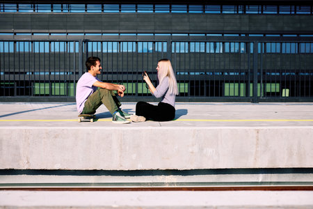 A happy teenage couple is sitting at the train station and taking photos.の写真素材