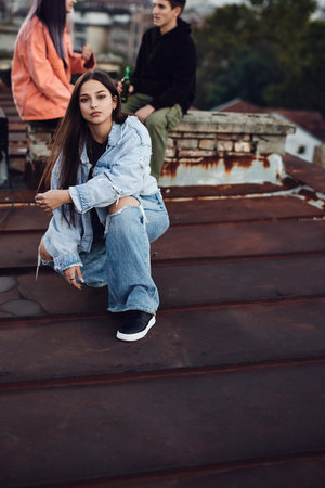 A girl posing and kneeling on the rooftop while her friends sitting in the background and drinking beer.の写真素材