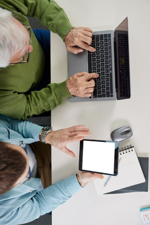 Young educator showing senior student how to solve a problem on project on his tablet while the student typing on a laptop.の写真素材
