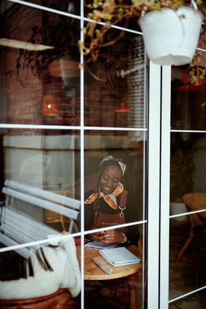 View through the window on young hipster african american woman studying in the internet cafe.