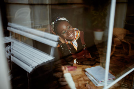 A smart African college girl sits in the cafeteria and studies for an exam. The picture was taken from the outside. A girl on student exchange sitting in a coffee shop and studying.の写真素材