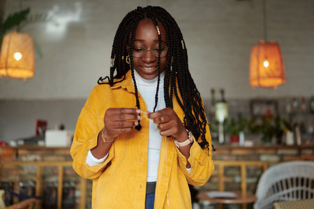 A smiling african american girl with braids looking at jewelery in cafe.の写真素材