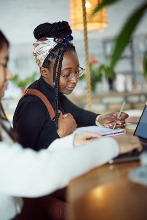 Two multicultural female students sit in a coffee shop and study for the final exam.の写真素材