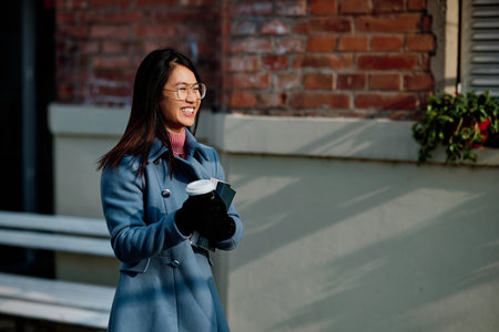 A happy multiracial young woman is standing outside and holding coffee and books she wants to read.の写真素材