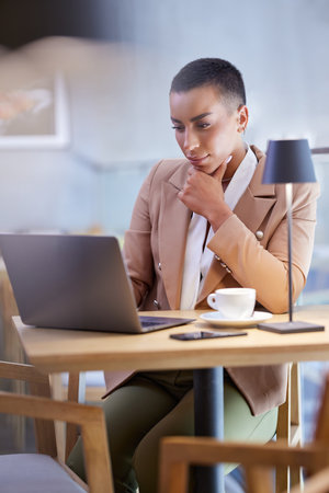 A focused businesswoman finishes paperwork on a laptop in a working friendly cafe.の写真素材