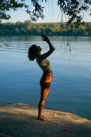 A fit yogi woman standing on a lake shore and doing a sun salutation.の写真素材