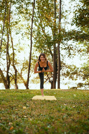 A happy woman is practicing yoga in the forest. She is balancing on one leg.の写真素材