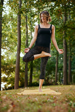 A slim woman practices yoga in the forest in autumn. She is in the Standing Half Lotus yoga pose.の写真素材