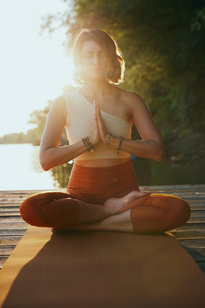 A woman meditates in a lotus position on a dock at sunset.の写真素材