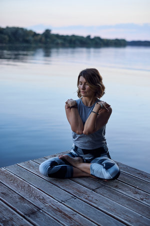 A calm yogi woman in a lotus position is meditating on the dock.の写真素材