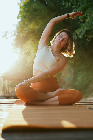 A calm woman in the lotus pose sits on a dock and practices yoga breathing near the river.の写真素材