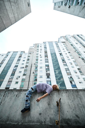 A teenage boy is lying down on the concrete wall surrounded by buildings.の写真素材