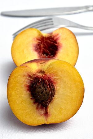 variety of fruit with a large pit and soft pinkish flesh; color peach, yellowish-orange color, diffuse background with a fork and knifeの写真素材