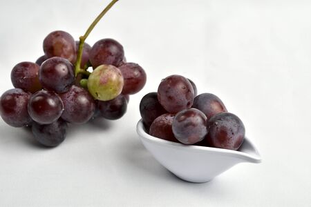 Grapes placed in a saucer, on a white tablecloth, as a background a cluster of diffuse grapesの写真素材