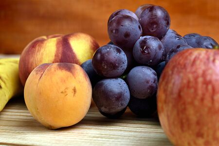 Seasonal fruits which are: peach, grapes, apple, banana, mango, placed on a wooden table and with a diffuse background of dark woodの写真素材