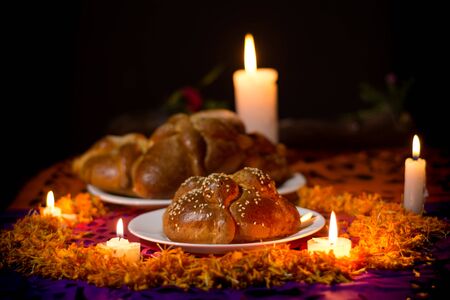 pan de muerto, placed on white plates, adorned with cempasuchil petals and burning candles around it. Dark diffuse backgroundの写真素材