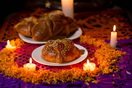 pan de muerto, placed on white plates, adorned with cempasuchil petals and burning candles around it.の写真素材