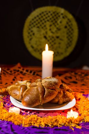 Pan de muerto traditional recipe from Mexico, adorned with candles and cempasuchil flower petals, in the background chopped papael and candle commemorating the Day of the Deadの写真素材