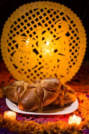 Pan de muerto traditional recipe from Mexico, adorned with candles and cempasuchil flower petals, in the background chopped papael and candle commemorating the Day of the Deadの写真素材