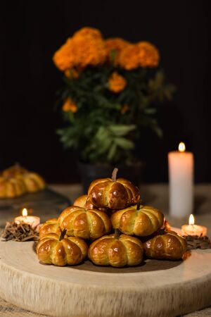 Pumpkin bread, placed in a pyramid, around a candle and cempazuchitl flower, next to a natural pumpkin. In the background pumpkin bread and a pot of cempazuchitl flowersの写真素材