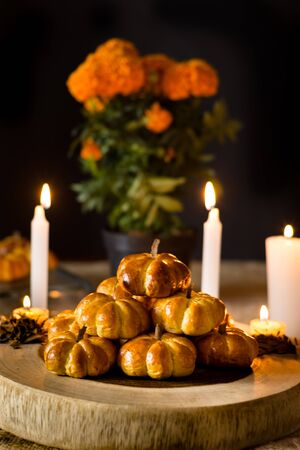 Pumpkin bread, placed in a pyramid, around a candle and cempazuchitl flower, next to a natural pumpkin. In the background pumpkin bread and a pot of cempazuchitl flowersの写真素材