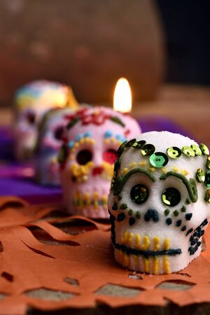 Skulls made by hand, made of sugar, decorated with colored glass and sequins, behind a lit candle. Placed in confetti and wood. Days of the dead Mexican traditionの写真素材