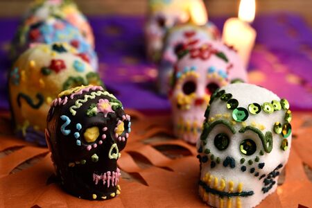 Skulls made by hand, made of sugar, decorated with colored glass and sequins, behind a lit candle....