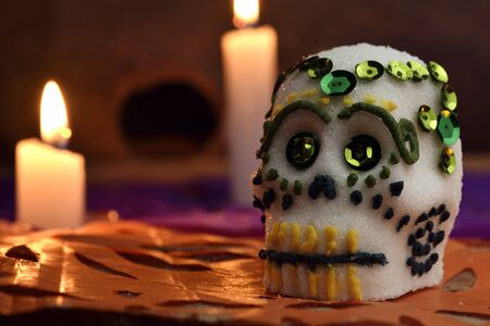 Skull made by hand, made of sugar, decorated with colored glass and sequins, behind some burning candles. Placed in confetti and wood. Days of the dead Mexican traditionの写真素材