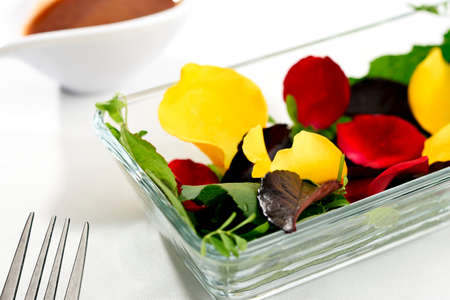 Salad with rose petals, including rose leaves, lentils and beans, and wild leaves. In the background a dressing in a bowlの写真素材