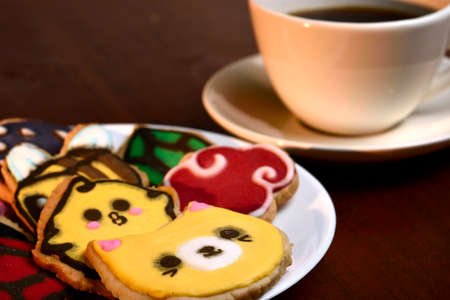 Cookies made with butter and decorated with various figures such as a cat, chicken, bee, mushrooms, placed on a glass plate and a wooden base, diffuse bottom of a cup of coffee.の写真素材