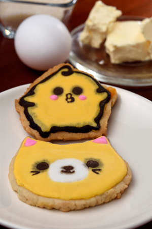 Cookies made with butter and decorated with various figures such as a cat and a chick, placed on a glass plate and a wooden base.の写真素材