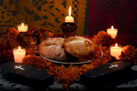 Traditional and sugary bread of the dead, around it marigold flowers, cardboard coffin, lighted candles, diffused confetti background.の写真素材