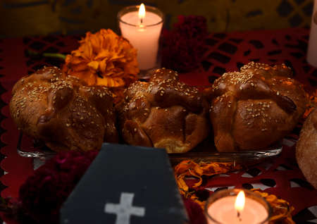 Traditional dead bread with sesame seeds, placed on a glass plate, around marigold flowers, burning candles and a cardboard coffin.の写真素材