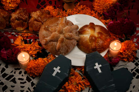 Traditional and sugary bread of the dead, around it marigold flowers, cardboard coffin, lighted candles, diffused confetti background.の写真素材