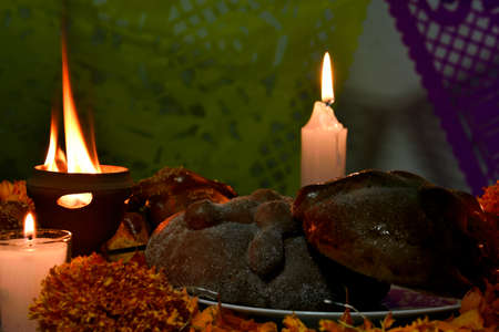 Traditional and sugary bread of the dead, around it marigold flowers, burning candles, diffuse background of colored confetti.の写真素材