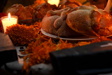 Traditional and sugary bread of the dead, around it marigold flowers, cardboard coffin, lighted candles, diffused confetti background.の写真素材