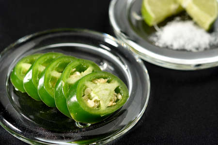 JalapeÃ±o chili pepper cut into slices and placed on a glass plate, in the bottom a lemon cut into two parts and salt.の写真素材