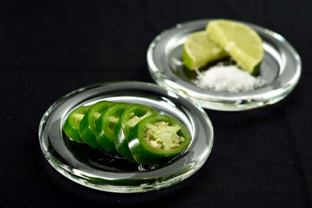 JalapeÃ±o chili pepper cut into slices and placed on a glass plate, in the bottom a lemon cut into two parts and salt.の写真素材