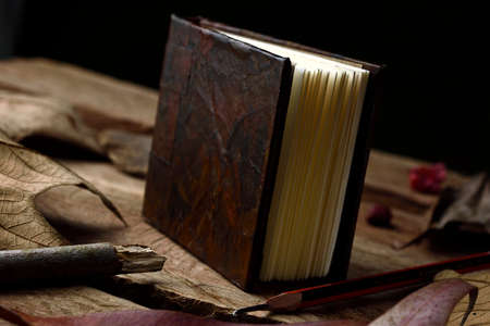 Notebook placed vertically in an imitation leather design, old style, decorated with still life that are leaves and wooden stick, placed on a wooden base.の写真素材
