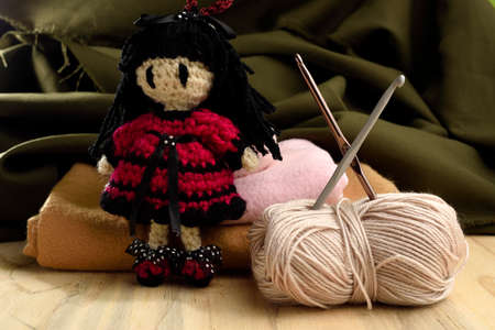 doll made with yarn, around it sewing needles, yarn and fabric, placed on Woodの写真素材