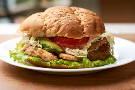 hamburger type sandwich with ingredients that are chicken milanesa, lettuce, string cheese, tomato and avocadoの写真素材