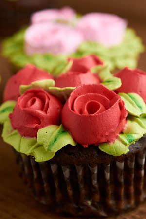 cupcake decorated with chantilly with rose design, placed on a wooden base, diffuse background of more cupcakeの写真素材