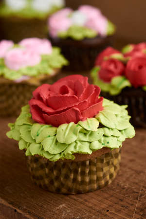 cupcake decorated with chantilly with rose design, placed on a wooden base, diffuse background of more cupcakeの写真素材